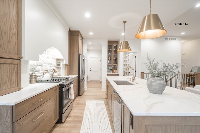 kitchen featuring stainless steel appliances, sink, hanging light fixtures, a spacious island, and light wood-type flooring