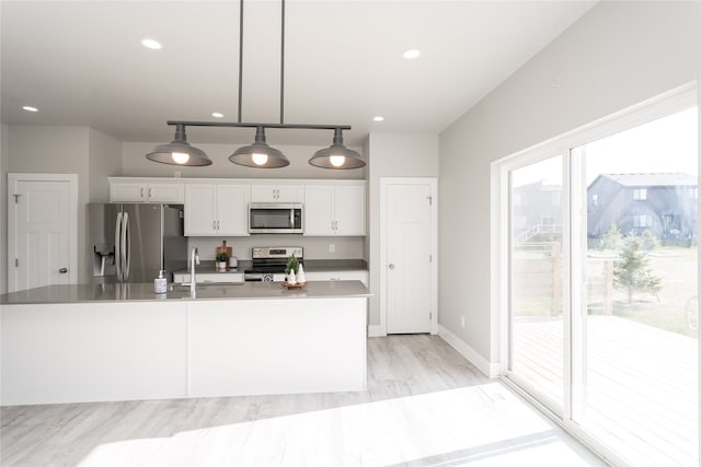 kitchen with light wood-type flooring, stainless steel appliances, sink, white cabinets, and hanging light fixtures