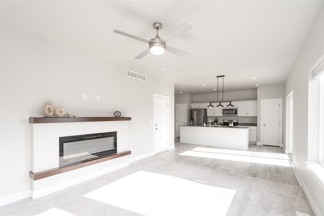 unfurnished living room featuring ceiling fan and light colored carpet