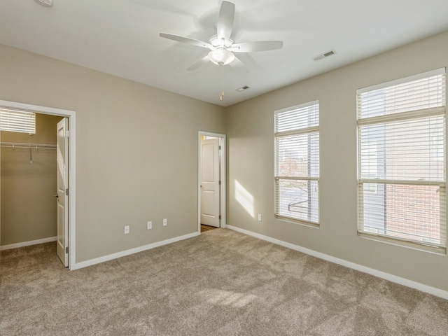 unfurnished bedroom featuring a closet, a spacious closet, light carpet, and ceiling fan