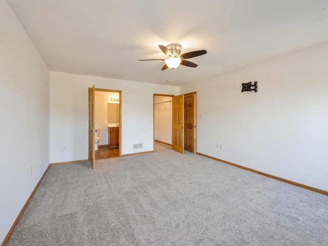 unfurnished bedroom with connected bathroom, carpet, ceiling fan, a closet, and a walk in closet