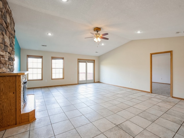 unfurnished living room featuring a stone fireplace, vaulted ceiling, a textured ceiling, light tile patterned floors, and ceiling fan