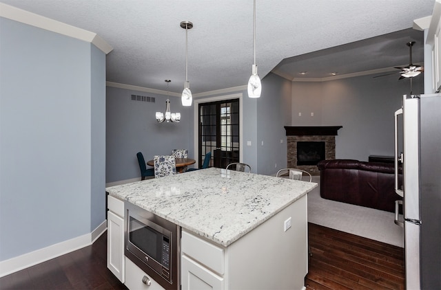 kitchen featuring stainless steel appliances, dark wood-type flooring, white cabinets, a fireplace, and decorative light fixtures