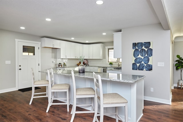 kitchen with light stone countertops, white cabinets, stainless steel dishwasher, and dark hardwood / wood-style floors