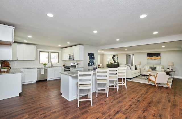 kitchen featuring white cabinetry, light stone countertops, dark hardwood / wood-style floors, a kitchen island, and appliances with stainless steel finishes