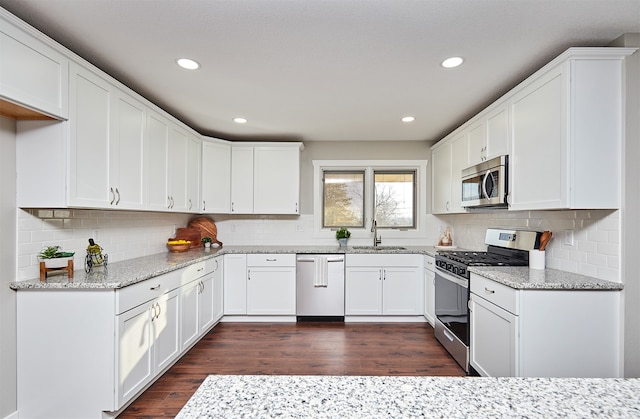 kitchen with appliances with stainless steel finishes, dark hardwood / wood-style flooring, light stone counters, sink, and white cabinetry