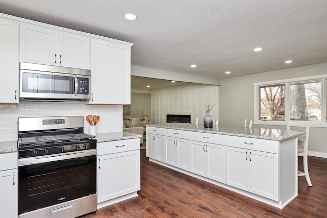 kitchen featuring dark hardwood / wood-style flooring, white cabinetry, light stone counters, and appliances with stainless steel finishes