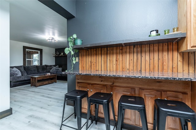 kitchen featuring dark stone countertops, light wood-type flooring, kitchen peninsula, and a kitchen bar