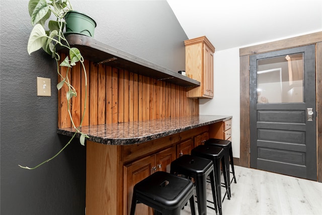 kitchen featuring dark stone countertops, a kitchen bar, and light hardwood / wood-style flooring