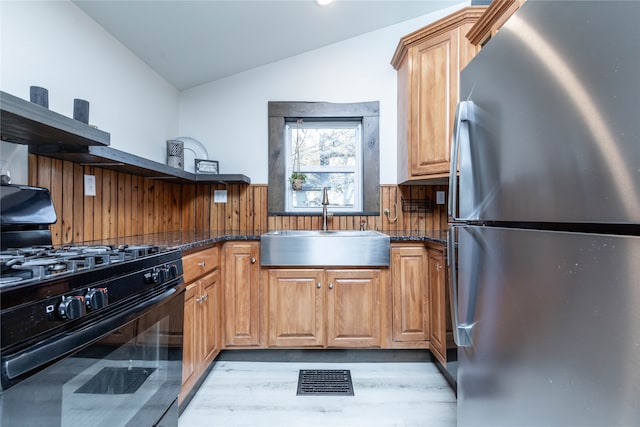 kitchen with vaulted ceiling, black gas stove, sink, light wood-type flooring, and stainless steel fridge