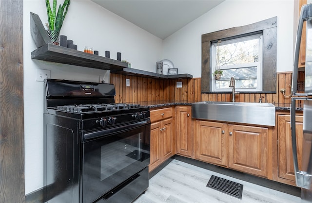 kitchen featuring lofted ceiling, sink, light hardwood / wood-style flooring, black gas range oven, and dark stone countertops