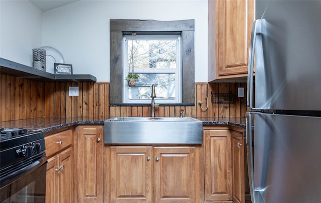 kitchen with stainless steel refrigerator, dark stone countertops, sink, and black range with electric cooktop