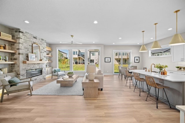 living room with a fireplace, sink, ceiling fan, and light hardwood / wood-style flooring