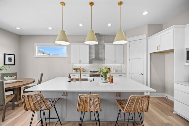 kitchen featuring light hardwood / wood-style floors, decorative light fixtures, a center island with sink, and wall chimney range hood