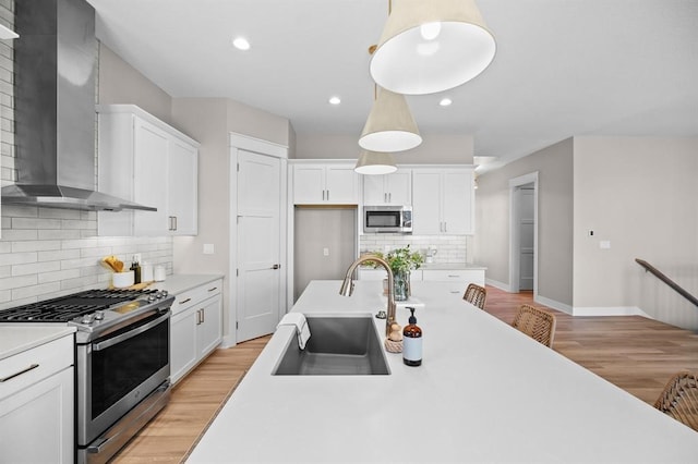 kitchen featuring white cabinetry, sink, appliances with stainless steel finishes, wall chimney range hood, and pendant lighting