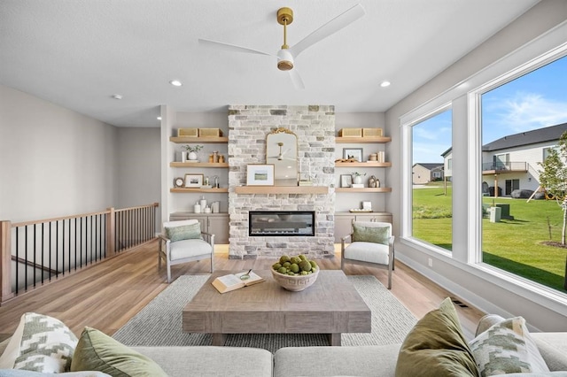 living room featuring ceiling fan, a stone fireplace, and light hardwood / wood-style flooring