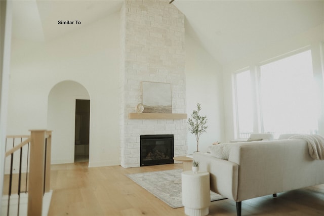 living room with a stone fireplace, light wood-type flooring, and high vaulted ceiling