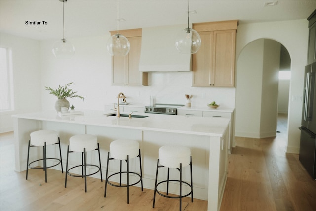 kitchen with hanging light fixtures, sink, range, light brown cabinets, and light hardwood / wood-style flooring