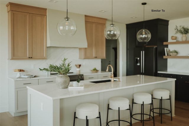 kitchen with hardwood / wood-style flooring, a center island with sink, sink, black refrigerator with ice dispenser, and white cabinets