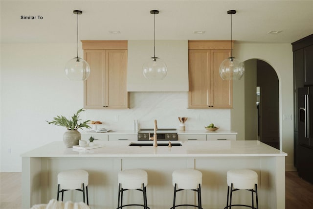 kitchen with black fridge, sink, a kitchen island with sink, light wood-type flooring, and light brown cabinetry