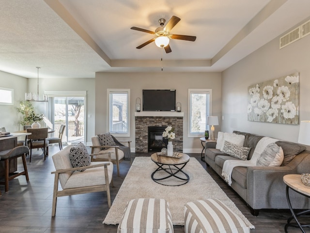 living room featuring dark wood-type flooring, a wealth of natural light, a stone fireplace, and ceiling fan with notable chandelier