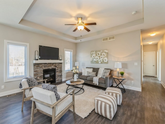 living room featuring ceiling fan, dark hardwood / wood-style floors, a raised ceiling, and a stone fireplace