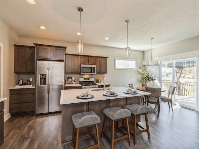 kitchen with a center island with sink, sink, dark hardwood / wood-style floors, appliances with stainless steel finishes, and decorative light fixtures