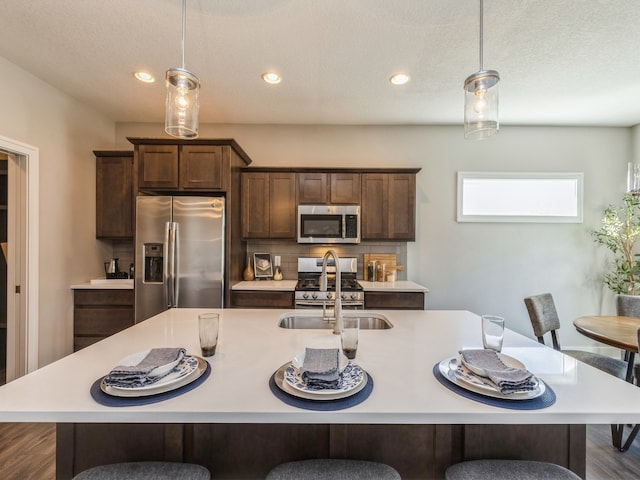 kitchen with a center island with sink, appliances with stainless steel finishes, a kitchen bar, hanging light fixtures, and sink