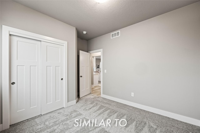 unfurnished bedroom with light carpet, a closet, and a textured ceiling