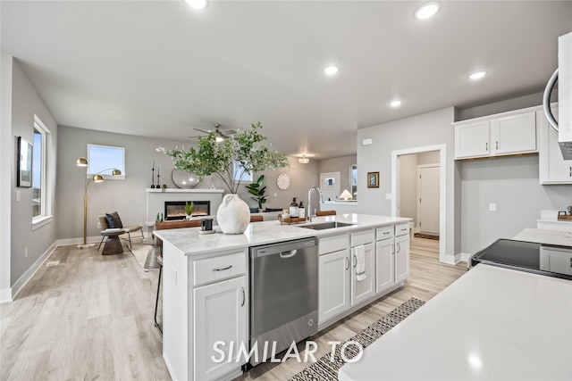 kitchen with sink, a center island with sink, stainless steel dishwasher, ceiling fan, and white cabinets