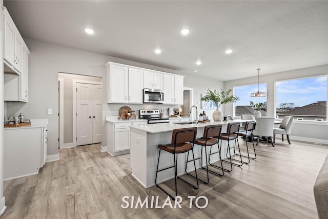 kitchen featuring decorative light fixtures, an island with sink, white cabinets, and appliances with stainless steel finishes