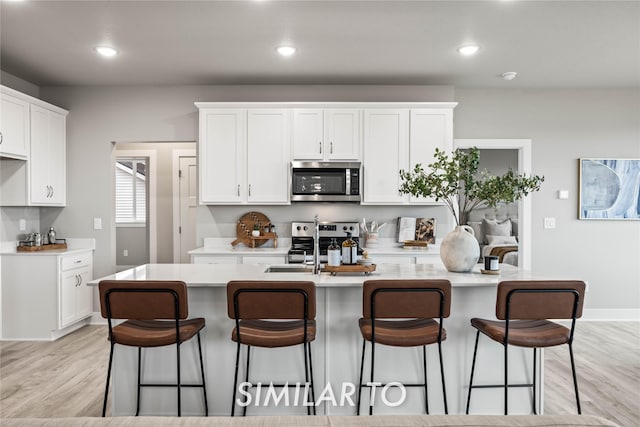 kitchen with stainless steel appliances, light hardwood / wood-style floors, an island with sink, and white cabinets