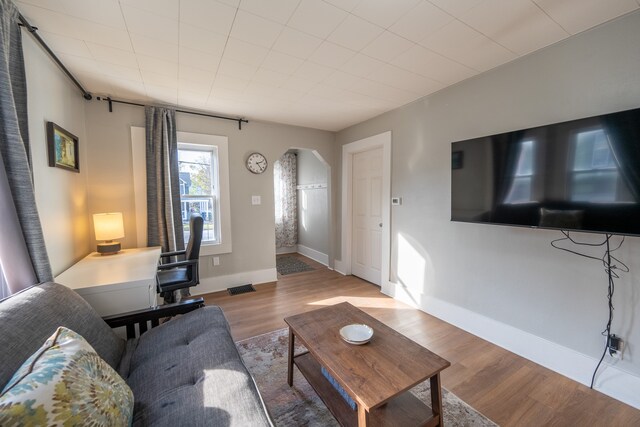 living room featuring arched walkways, baseboards, visible vents, and wood finished floors