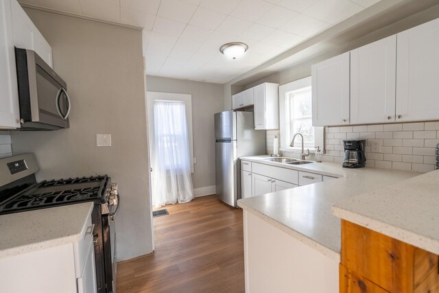 1215 21st St, Des Moines, IA 50311 - kitchen with stainless steel appliances, a sink, tasteful backsplash, wood finished floors, and white cabinetry