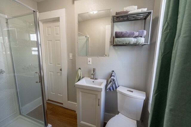 bathroom with vanity, toilet, wood finished floors, and a stall shower