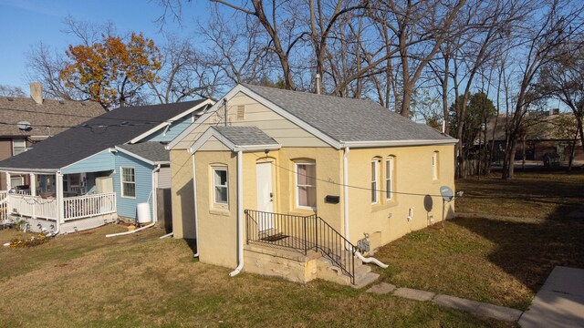 view of front facade featuring a shingled roof, stucco siding, and a front yard