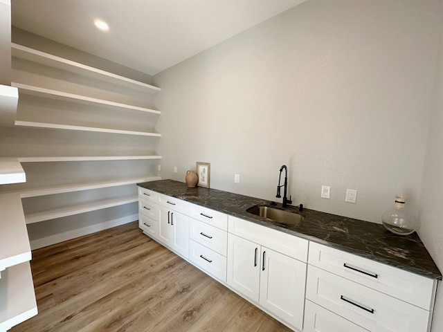 bar with white cabinetry, light hardwood / wood-style floors, dark stone counters, and sink