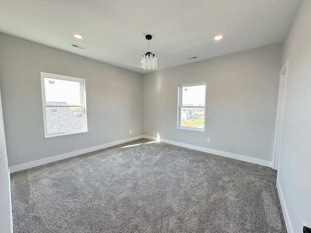 empty room featuring a wealth of natural light, an inviting chandelier, and carpet flooring