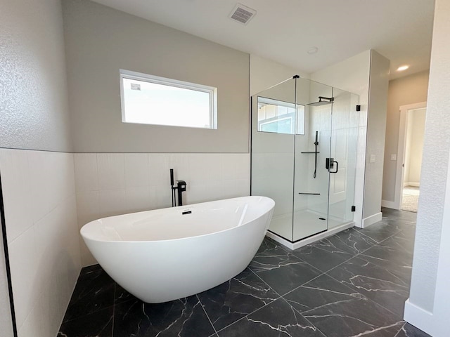 bathroom featuring shower with separate bathtub and tile walls