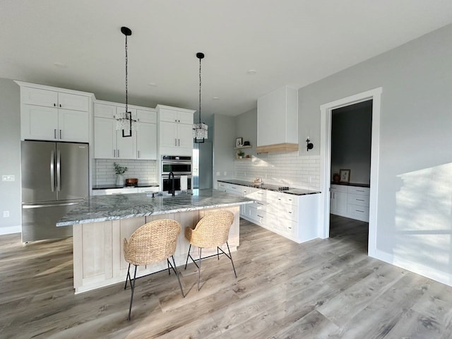 kitchen with tasteful backsplash, a center island with sink, white cabinetry, appliances with stainless steel finishes, and stone countertops