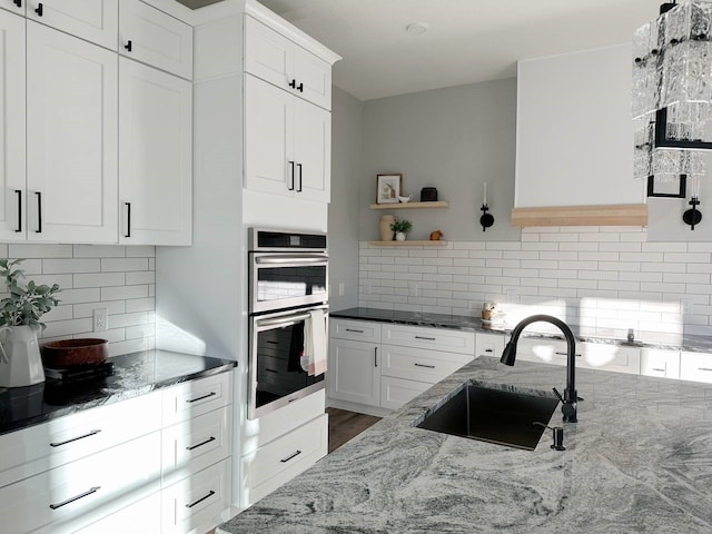 kitchen with decorative backsplash, white cabinetry, stainless steel double oven, and sink