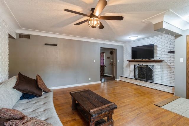 living room with a textured ceiling, hardwood / wood-style flooring, ceiling fan, and a brick fireplace