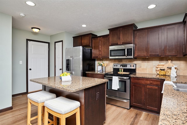 kitchen featuring light stone counters, light hardwood / wood-style floors, a textured ceiling, decorative backsplash, and appliances with stainless steel finishes