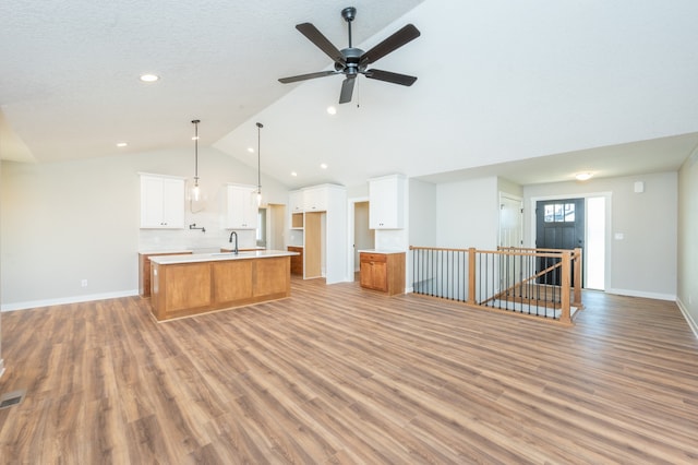 unfurnished living room featuring light wood-type flooring, lofted ceiling, sink, and ceiling fan