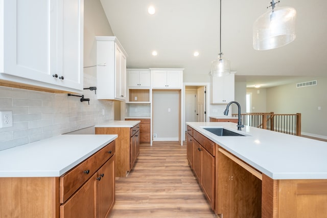 kitchen featuring pendant lighting, white cabinets, sink, and a kitchen island with sink