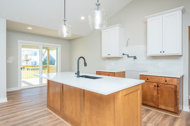 kitchen featuring sink, decorative light fixtures, an island with sink, white cabinets, and light wood-type flooring