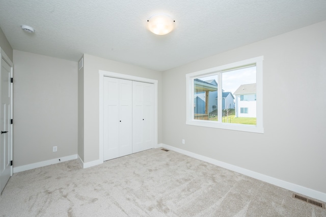 unfurnished bedroom with a textured ceiling, light carpet, and a closet