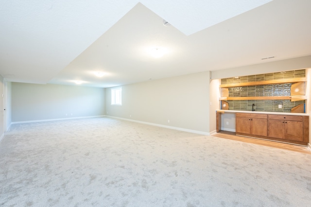 unfurnished living room featuring built in features, light carpet, and indoor bar