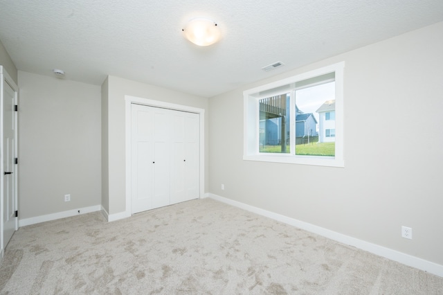 unfurnished bedroom featuring a textured ceiling, light carpet, and a closet