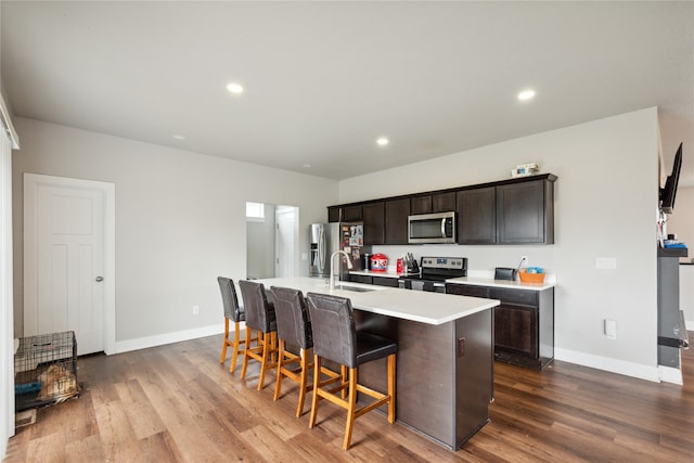 kitchen featuring a kitchen bar, wood-type flooring, sink, a kitchen island with sink, and appliances with stainless steel finishes